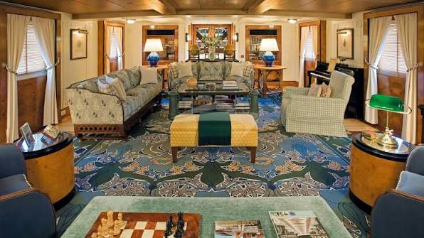 Saloon seen lengthways with green and blue furnishings, bookshelves and a piano