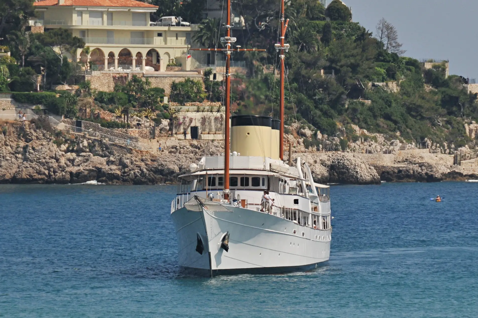 Talitha bow-on at anchor below a Mediterranean shoreline