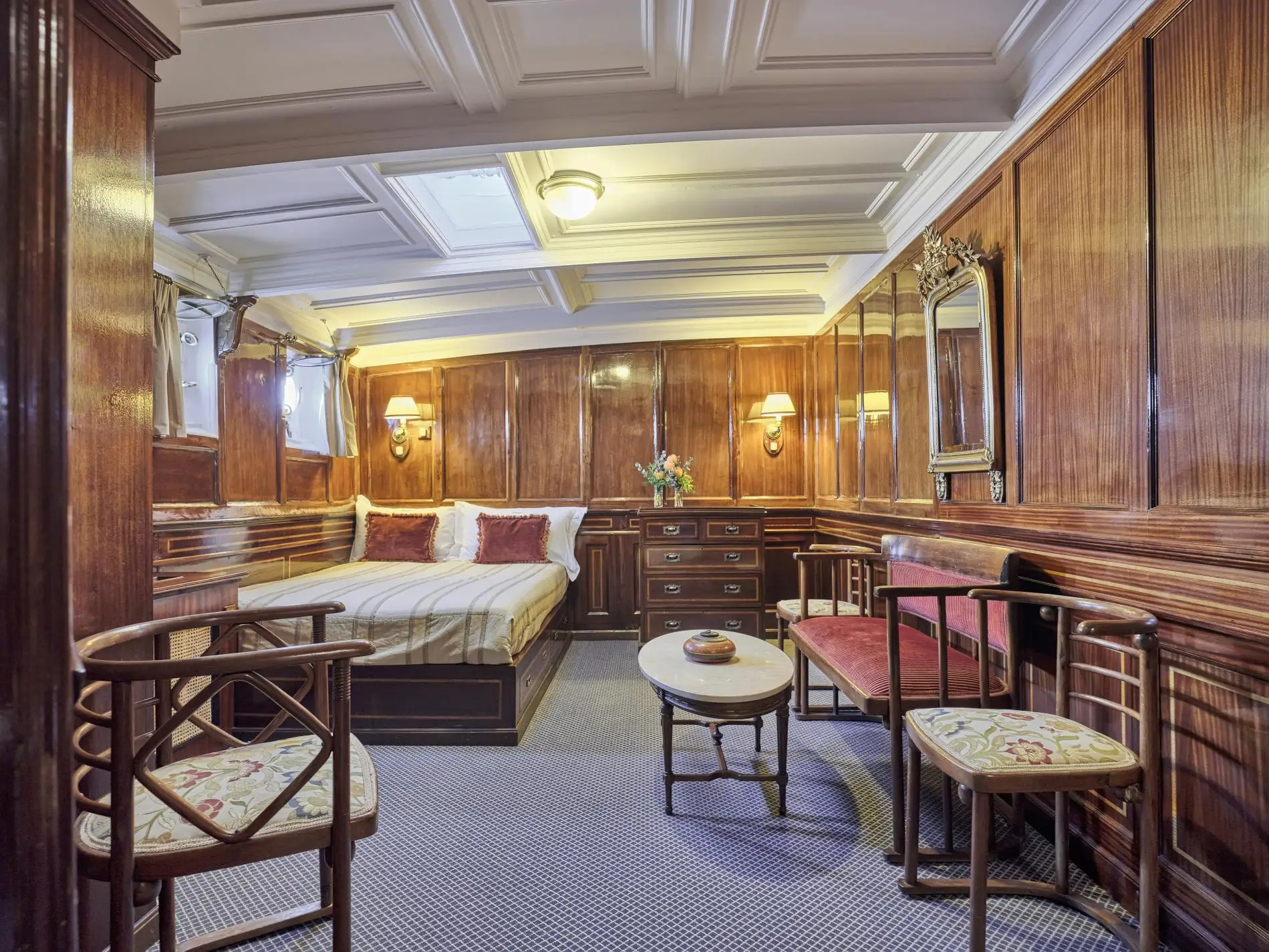 Mahogany-panelled stateroom with a coffered ceiling, double bed, chest of drawers and bentwood chairs