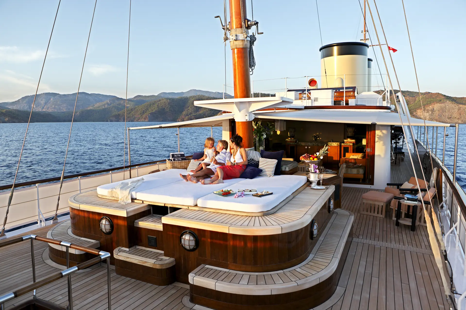 Sun deck daybed under the mast with a mountainous coast beyond