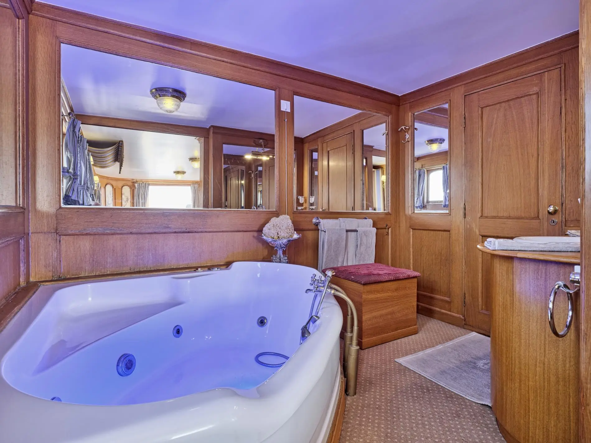 Panelled bathroom with a large corner bath, mirrors and a timber vanity unit