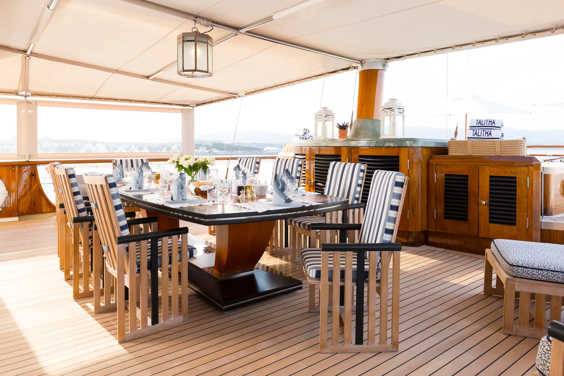 Long deck dining table with striped chairs beneath a canvas awning