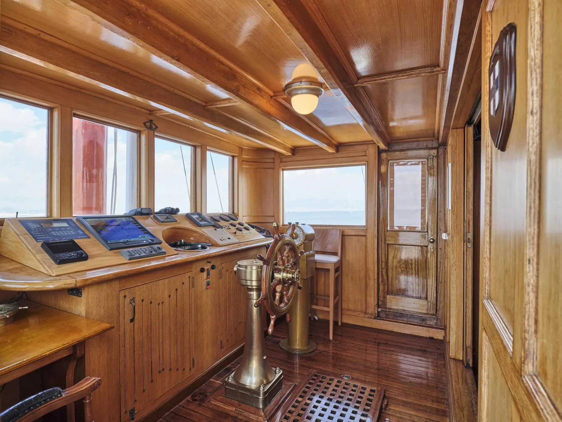 Varnished timber wheelhouse with a brass-capped ship's wheel, binnacle and contemporary navigation displays