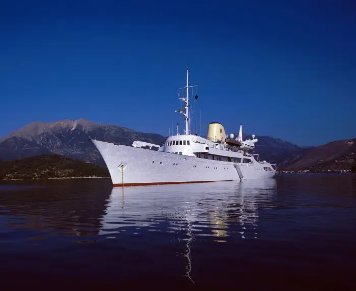 Christina O at anchor in blue water off a dry hillside coast
