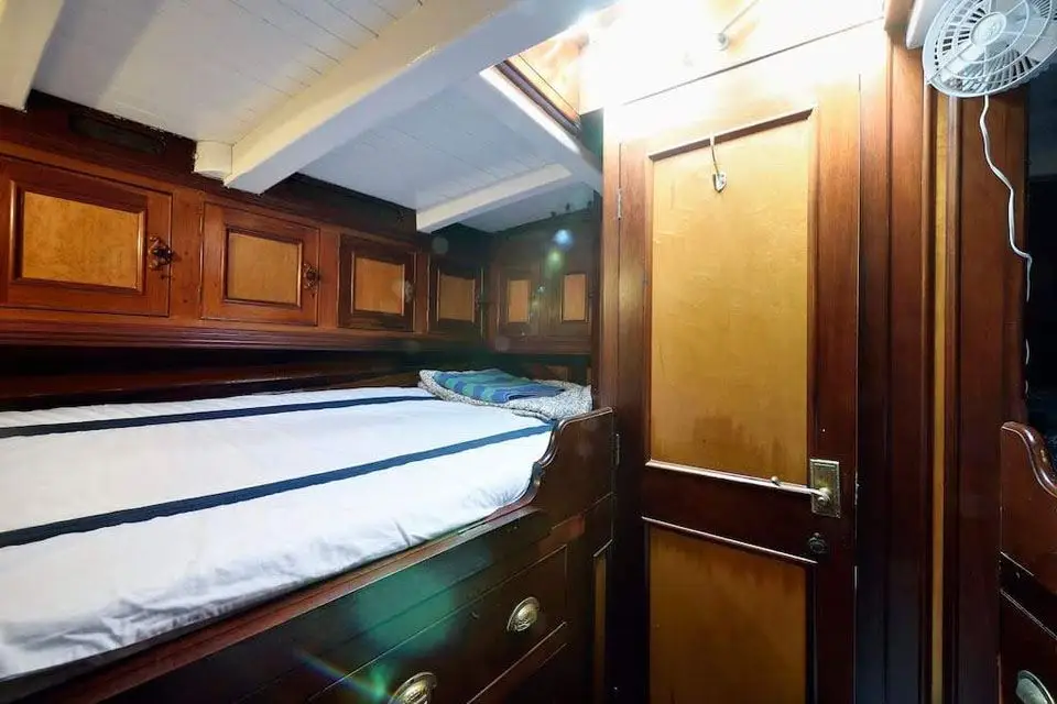 Narrow panelled cabin with a single berth, drawers and a burr-panelled door