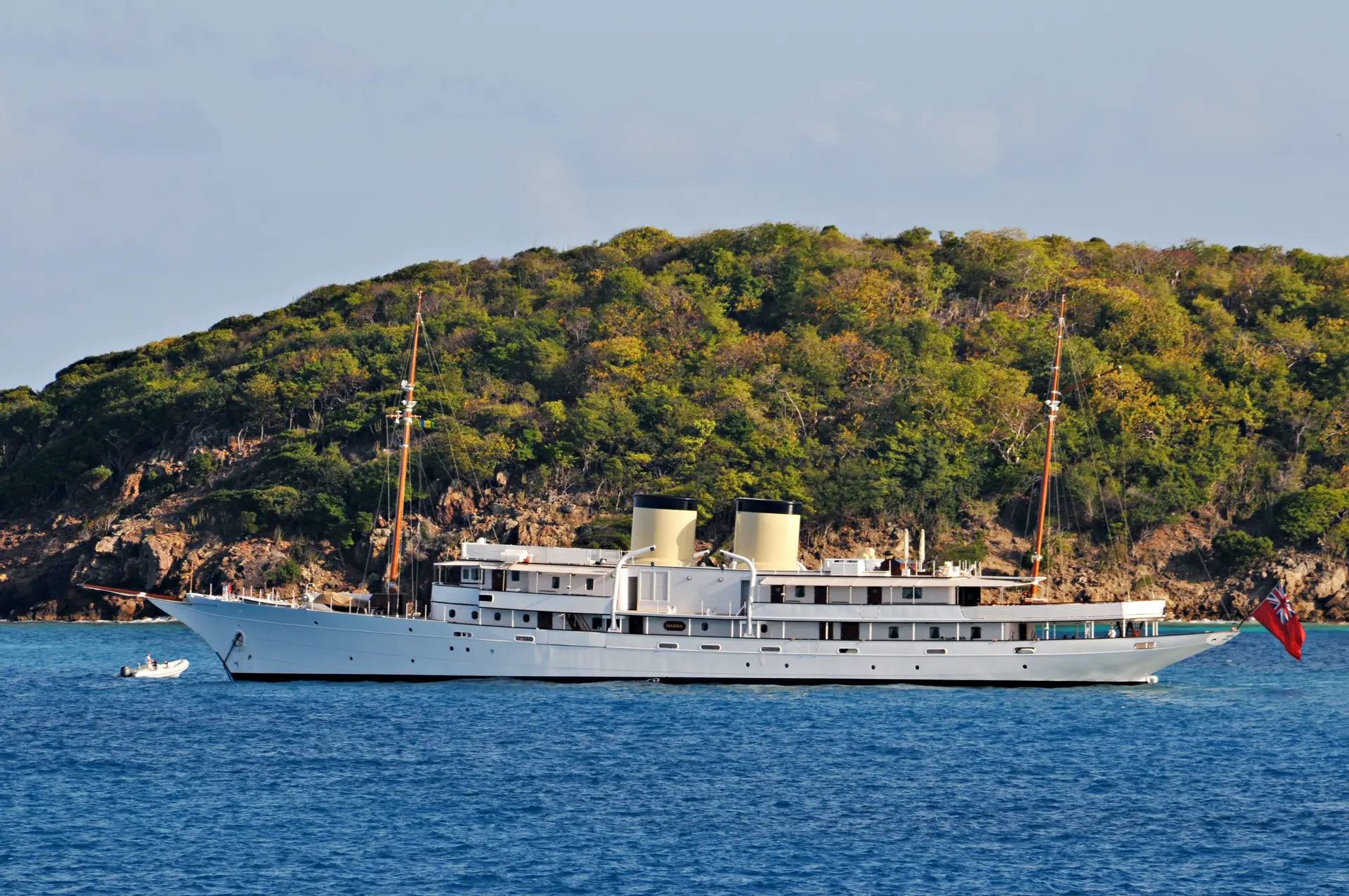 Talitha at anchor with a tender approaching, green hillside behind
