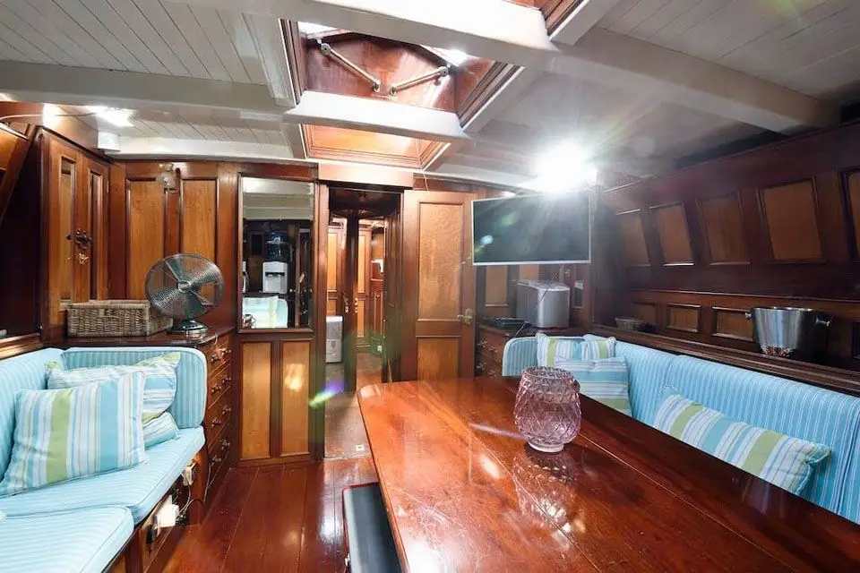 Panelled saloon with a long dining table, striped settees and painted deckhead beams
