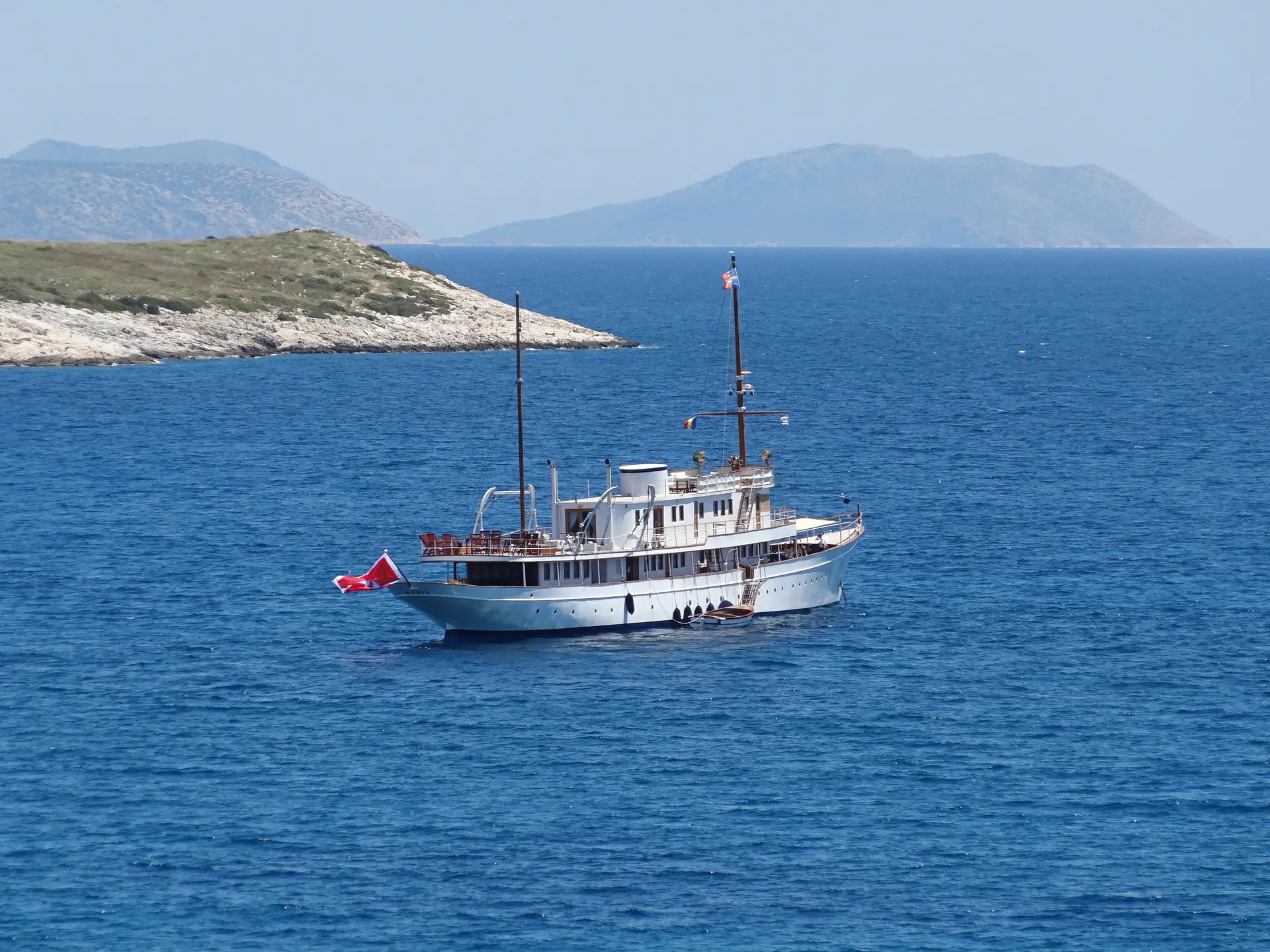 Distant view of Madiz anchored in deep blue water with islands behind