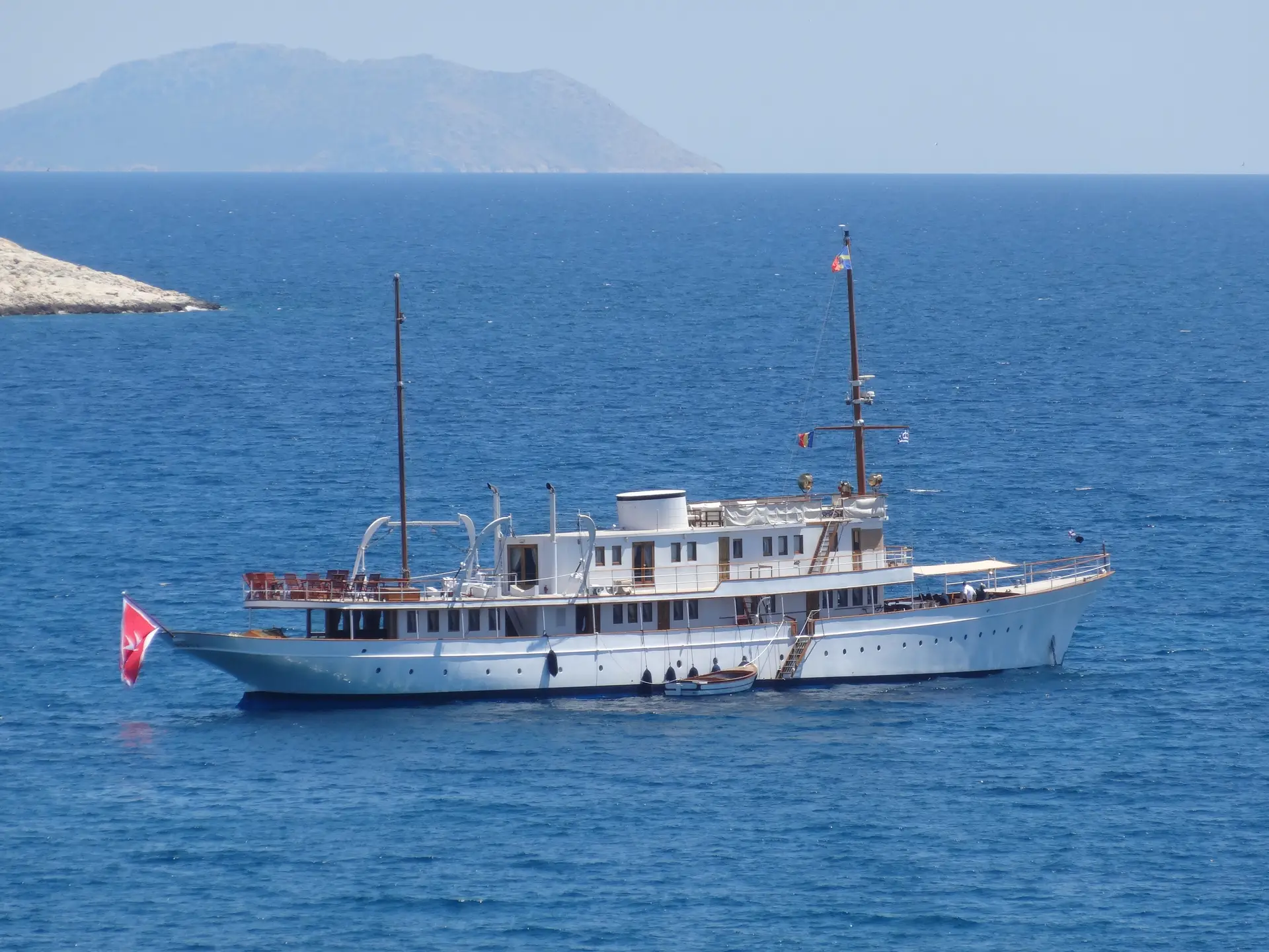Madiz at anchor in turquoise water below an arid hillside