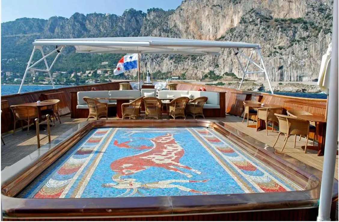 Circular mosaic swimming pool set into an open deck, with mosaic figures on the pool floor