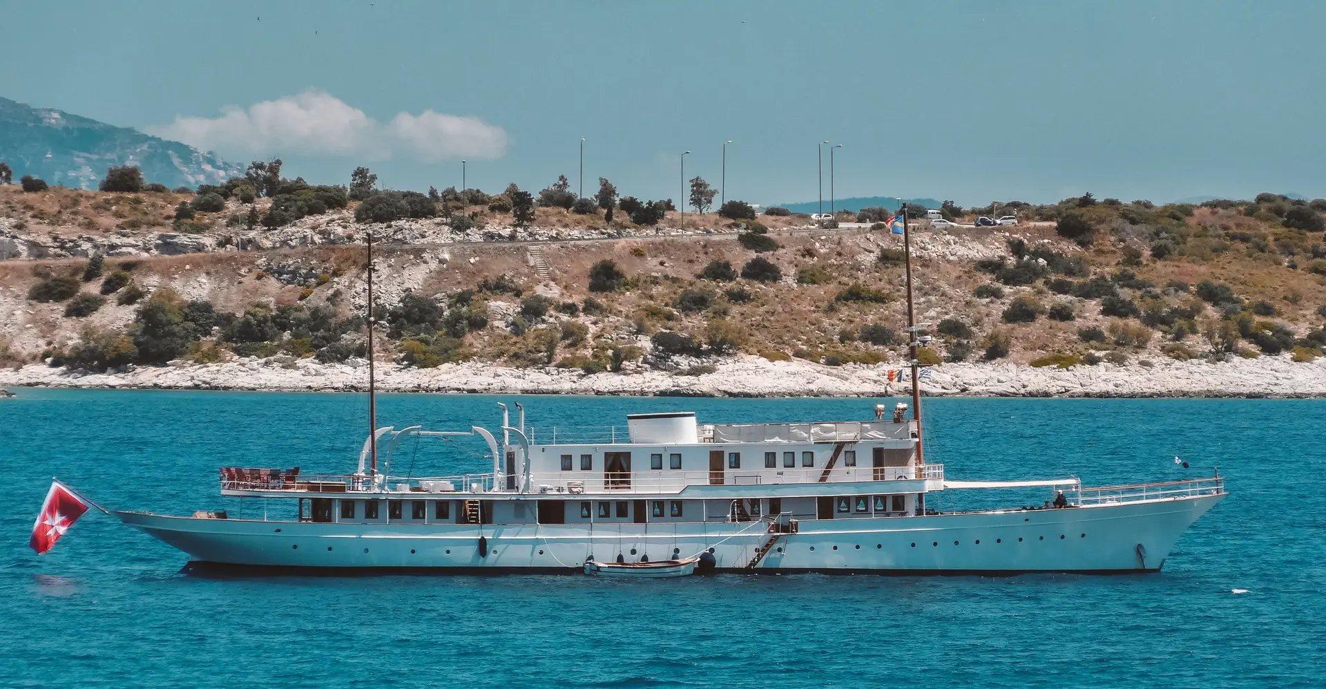Madiz anchored off a rocky Mediterranean shore with a tender alongside
